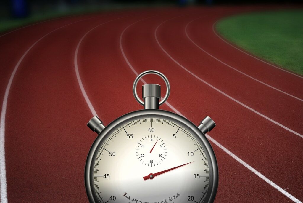 A stopwatch showing 30 seconds is in the foreground, with a red running track curving into the distance. The track has multiple lanes marked by white lines, and green grass can be seen adjacent to it.